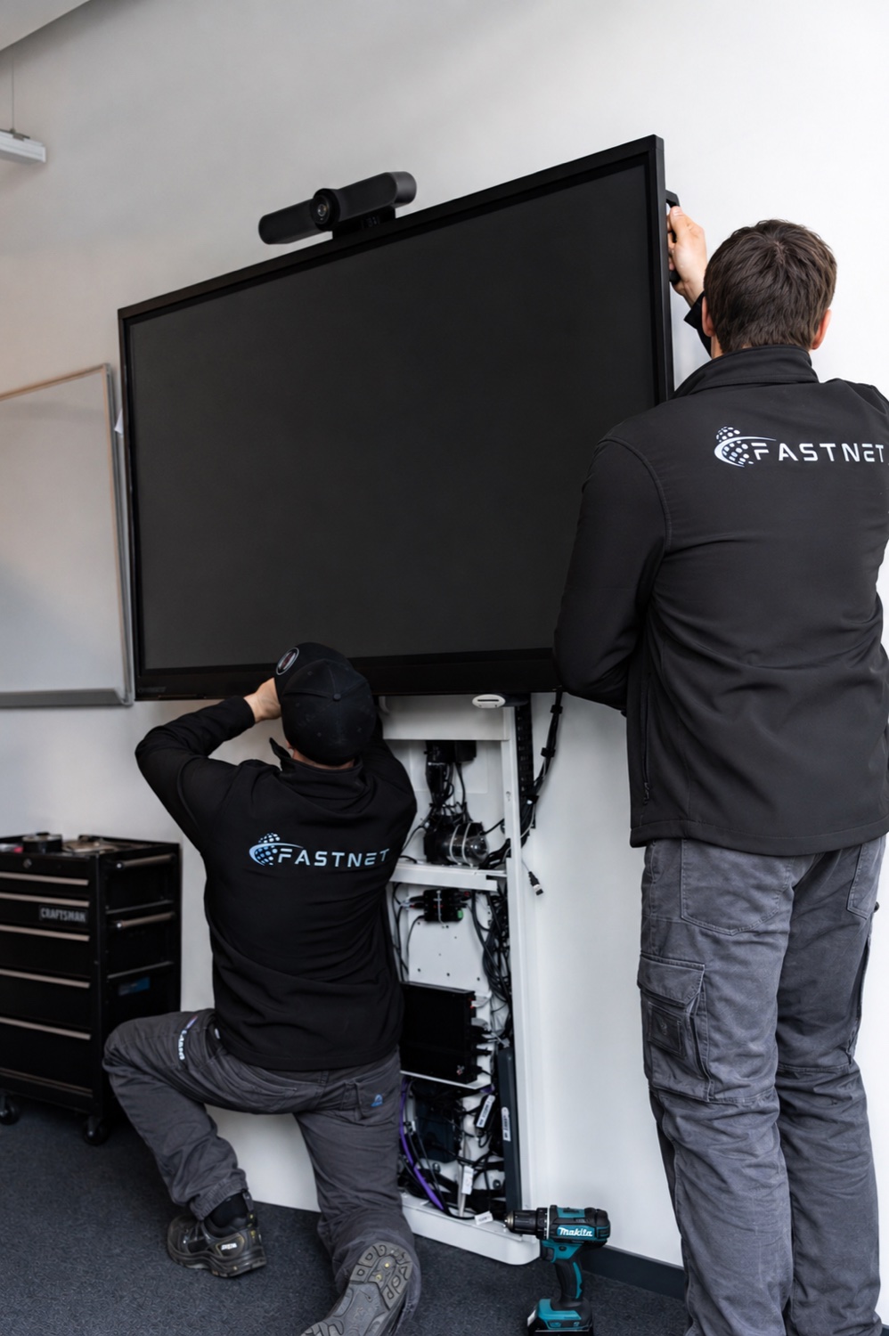FASTNET technician carrying out a professional smartboard wall installation with cable management in an existing building